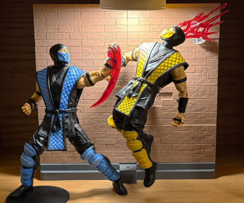 Two Mortal Kombat action figures posed mid-fight, with a blue-clad ninja slashing a yellow-clad ninja using a translucent red blood-splatter effect supported by a clear Bandai Stage Act stand.